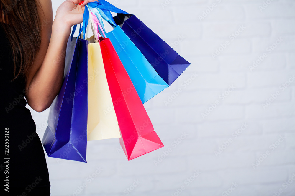 Shopping. Closeup of woman holding color paper shopping bag on white wall background