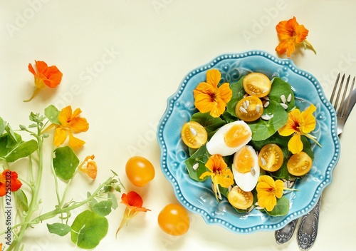 salad with nasturtium leaves and flowers of the plant. bright summer salad with edible yellow flowers and yellow tomatoes with egg, sunflower seeds and seasoned with olive oil. top view. copy space