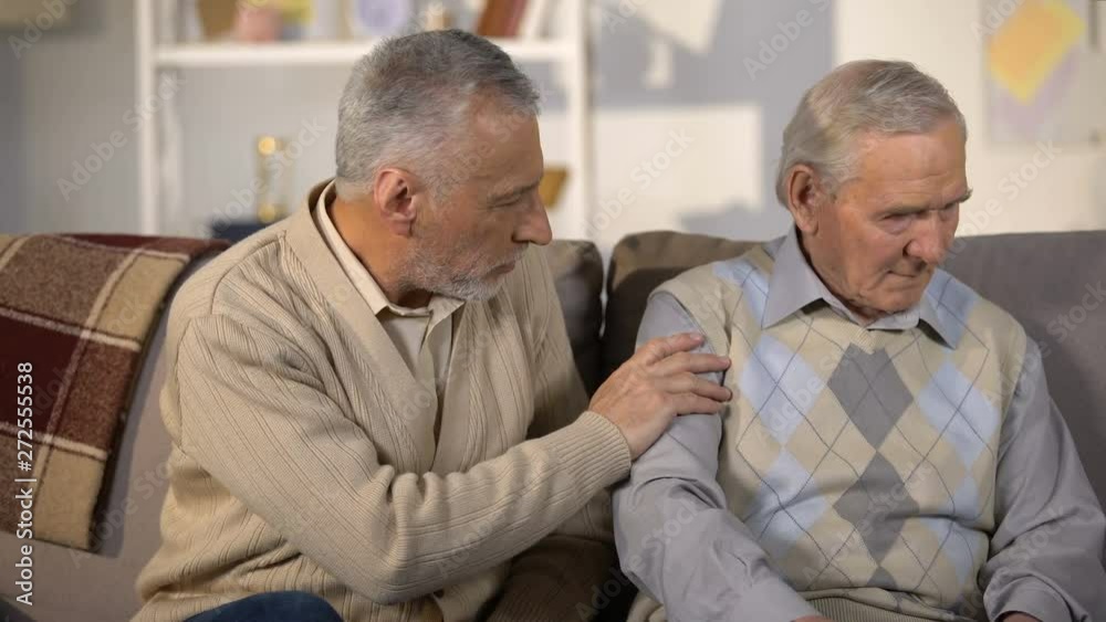Old man supporting upset friend, sitting on sofa at home, health problems Old man supporting upset friend, sitting on sofa at home, health problems