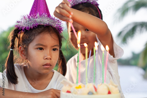 Two cute asian child girls lighting candle on birthday cake together in birthday party