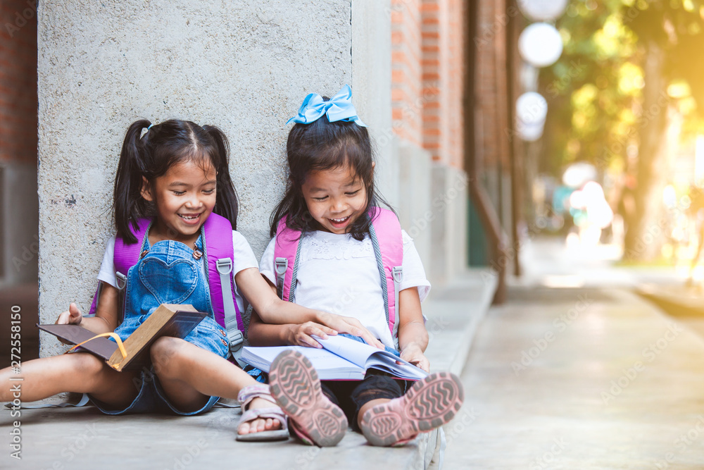 Back to school. Two cute asian pupil girls reading a book  together in the school with fun and happiness - obrazy, fototapety, plakaty 