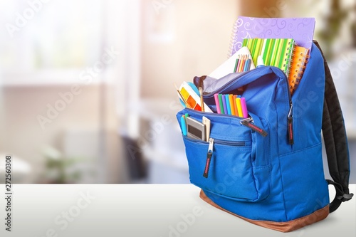 Open blue school backpack on a wooden desk and bokeh background.