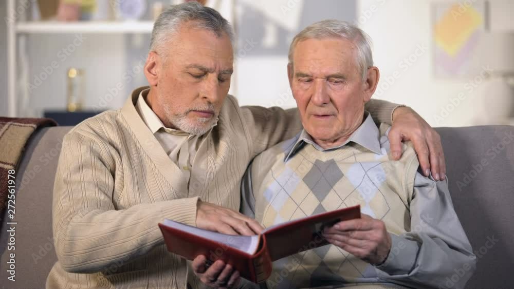 Old father and sun watching family album on sofa at home, togetherness, close-up Old father and sun watching family album on sofa at home, togetherness, close-up