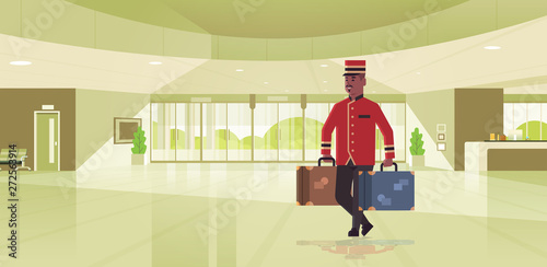 bell boy carrying suitcases hotel service concept african american bellman holding luggage male worker in uniform modern reception area lobby interior full length horizontal flat