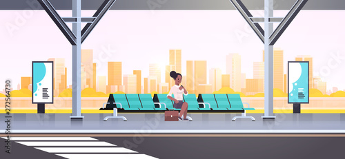 businesswoman sitting modern bus stop african american woman checking time waiting public transport on airport station cityscape background flat horizontal full length