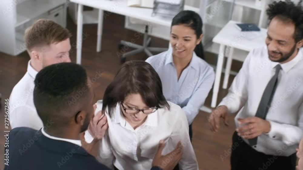 Handheld high angle tracking of happy office colleagues in formalwear standing in circle and catching laughing businesswoman in glasses trust falling on them while playing team building game in office Handheld high angle tracking of happy office colleagues in formalwear standing in circle and catching laughing businesswoman in glasses trust falling on them while playing team building game in office