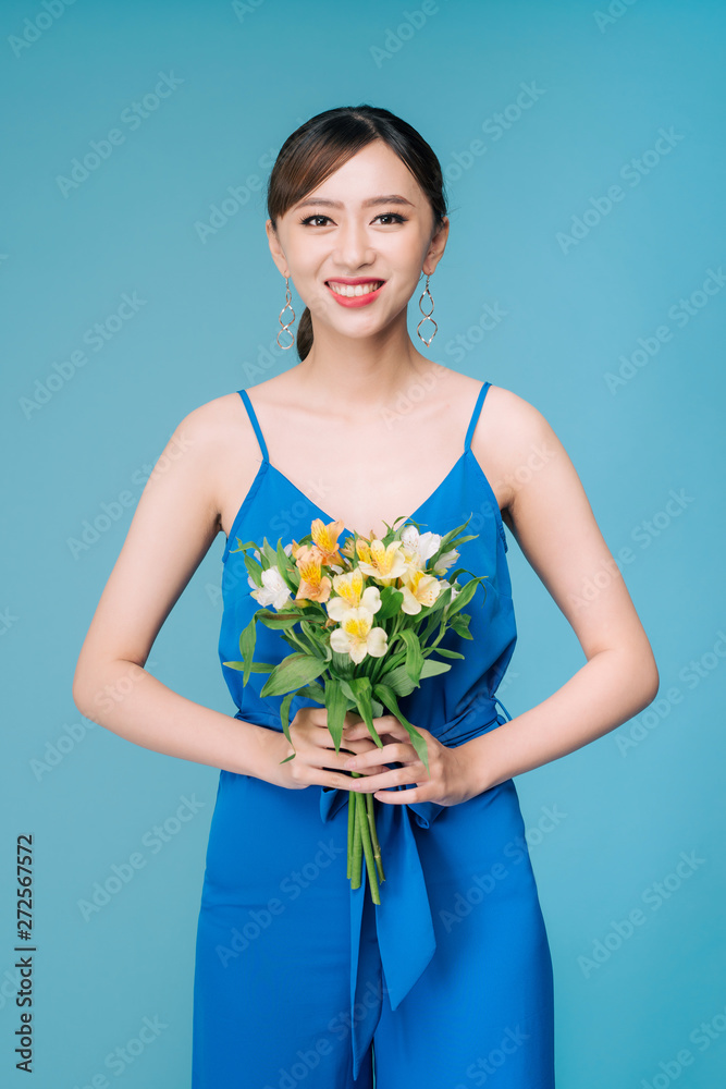 Attractive Asian woman in blue dress holding bouquet of flowers over blue background Attractive Asian woman in blue dress holding bouquet of flowers over blue background