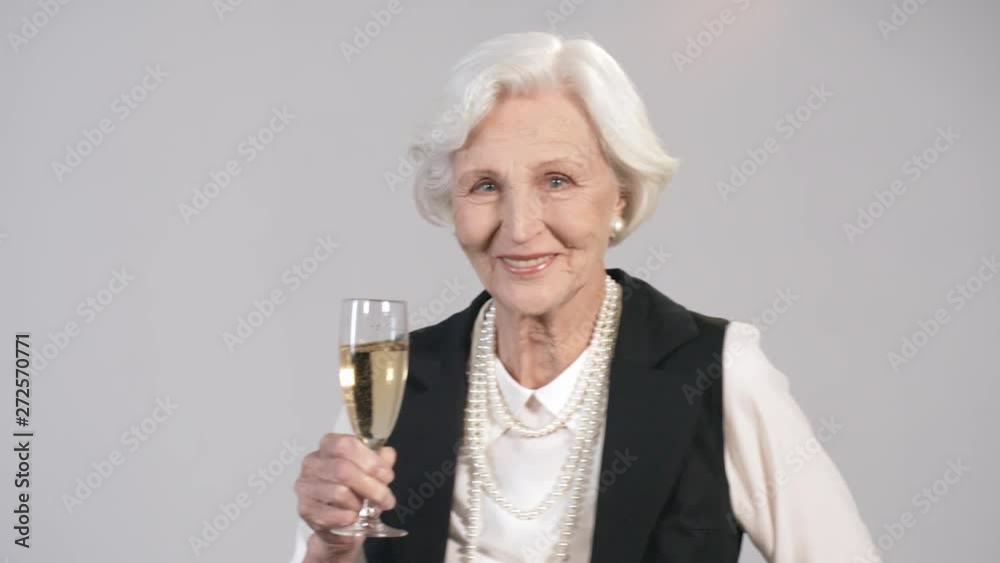 Portrait shot of happy elderly woman holding glass of champagne and dancing isolated on grey background Portrait shot of happy elderly woman holding glass of champagne and dancing isolated on grey background