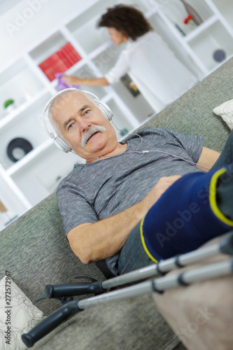 injured man listening to headphones woman doing chores in background