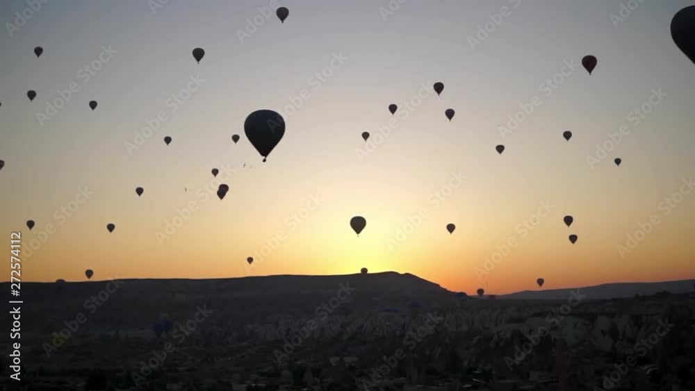 Backlit Balloons Rise High Above Rocks at Sunrise - Cappadocia, Turkey