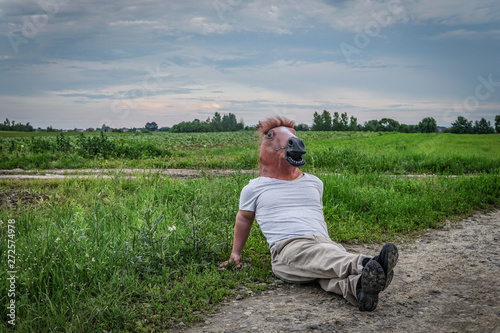 Man Wearing a Horse Mask Sitting in a Field
