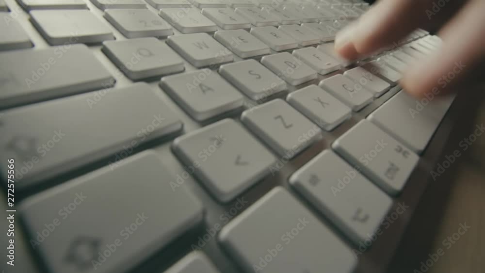 Close up view of silver computer keyboard with white keys and fingers typing. Person entering data into a computer. Fingers moving over keys and space bar. Dim light shines on metallic keyboard. Close up view of silver computer keyboard with white keys and fingers typing. Person entering data into a computer. Fingers moving over keys and space bar. Dim light shines on metallic keyboard.