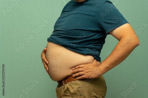 close up portrait of overweight obese man's hand holding his big belly