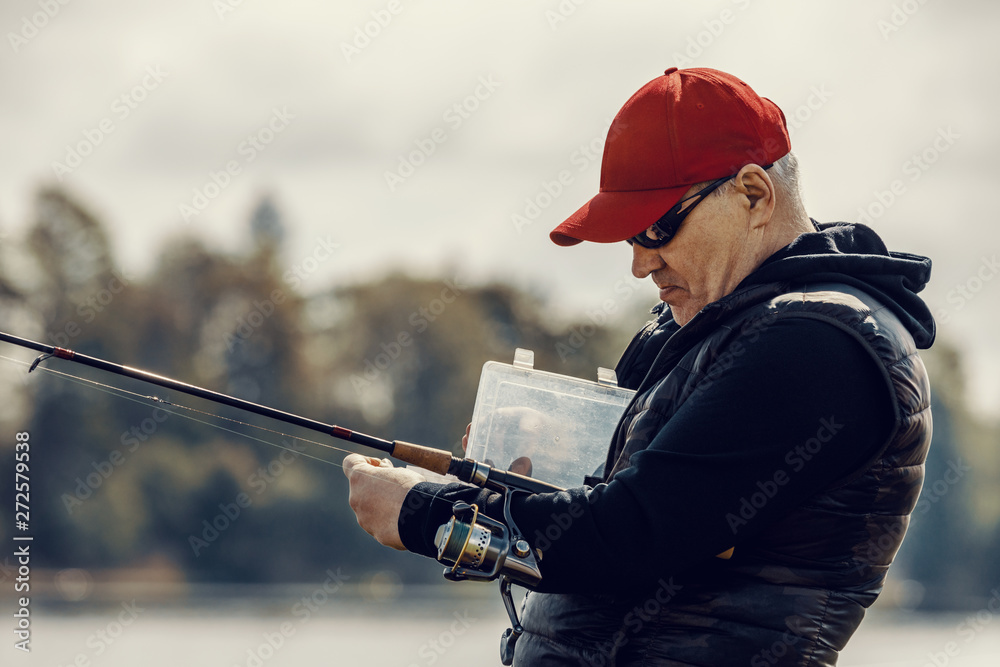Fototapeta premium Elderly man enjoys fishing by the river in the summer.