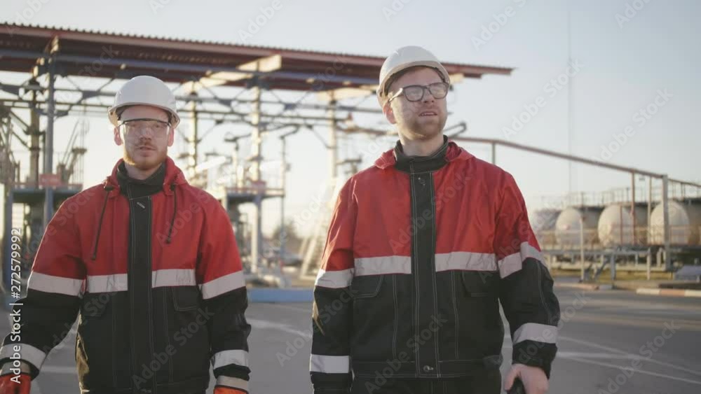 Two refinery oil engineers walk around sites of fuel company and discuss work Two refinery oil engineers walk around sites of fuel company and discuss work