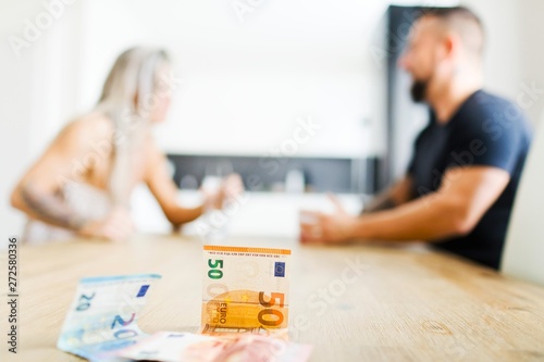 Man and woman sitting by table on opposite side and arguing - money