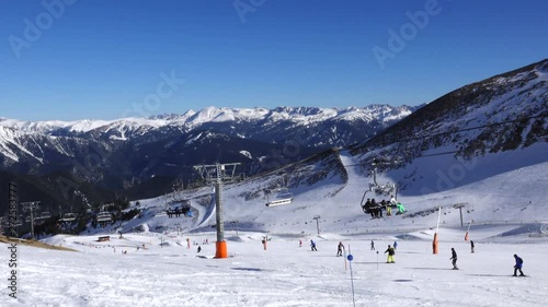 Panorama horizontal. Many people start skiing on a well-groomed ski slope at a ski resort. The sun is shining and the sky is bright and clear