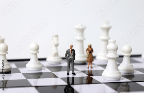 Miniature people standing and chess pieces on the chessboard.