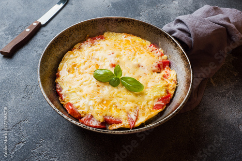 Omelet, scrambled eggs with tomatoes and cheese in a pan on a dark table.