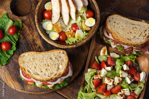 prosciutto sandwich, caprese, caesar salad on wooden plate close up