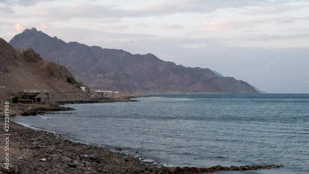 Beautiful clear water in Dahab Egypt. Exploring the blue water with mountains in the background and people windsurfing and kite surfing. Lady walking on the beach Beautiful clear water in Dahab Egypt. Exploring the blue water with mountains in the background and people windsurfing and kite surfing. Lady walking on the beach
