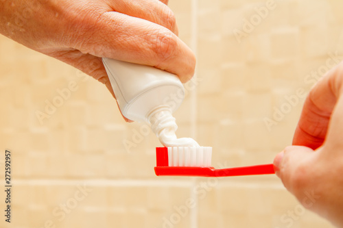 Red toothbrush and tube of toothpaste in female hands.
