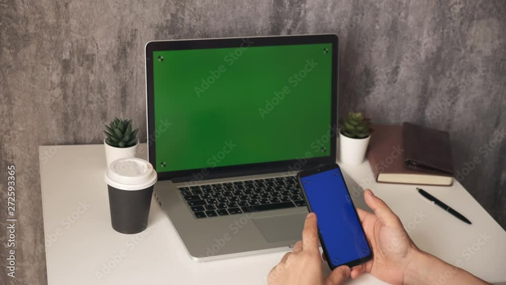A large plan for a laptop and a green-screen phone. man works with the phone. A young businessman in the office checks mail on the phone with a chroma key to insert A large plan for a laptop and a green-screen phone. man works with the phone. A young businessman in the office checks mail on the phone with a chroma key to insert