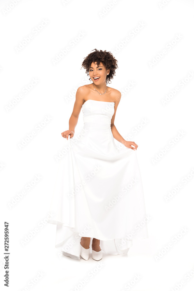 happy african american bride smiling while touching wedding dress isolated on white happy african american bride smiling while touching wedding dress isolated on white