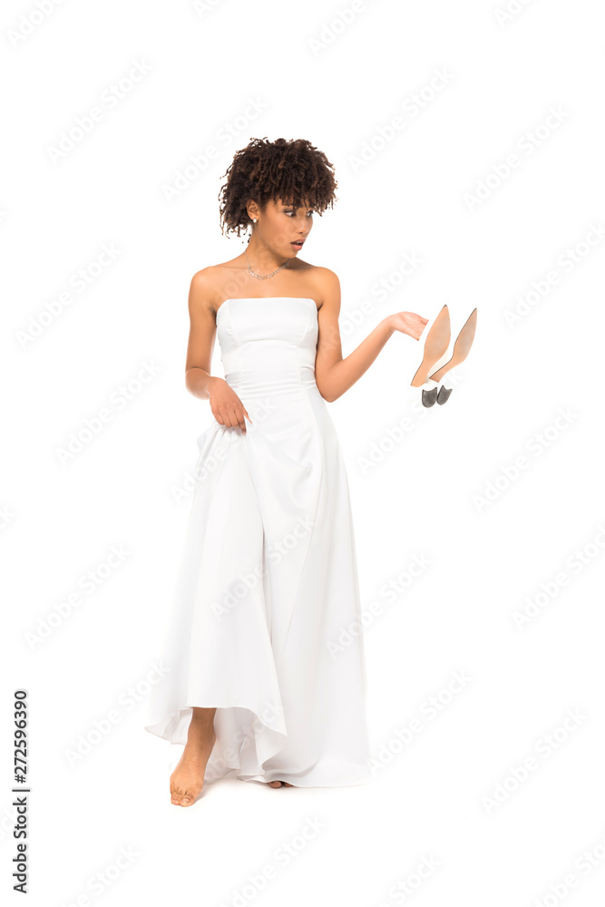 african american bride touching wedding dress and holding shoes while standing isolated on white african american bride touching wedding dress and holding shoes while standing isolated on white