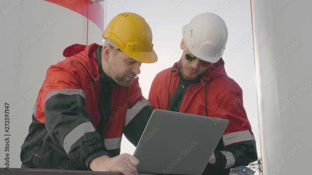 Two petrochemical engineers discuss data on laptop screen. Two petrochemical engineers discuss data on laptop screen.