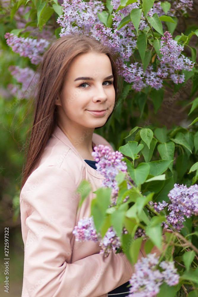 Young beautiful girl stands near the bushes of blooming lilac Young beautiful girl stands near the bushes of blooming lilac