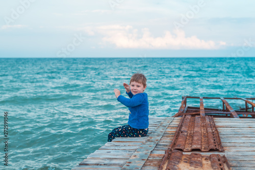 A little boy is sitting on the pier at sea.