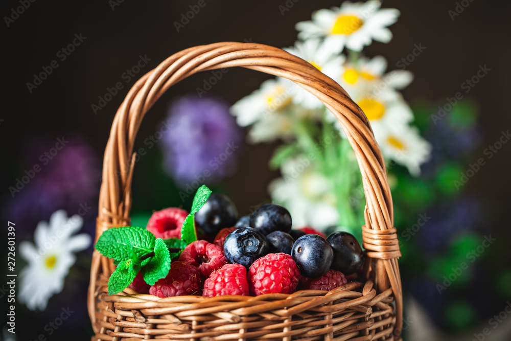 Raspberries and blueberries in a basket with chamomile and leaves on a dark background. Summer and healthy food concept. Selective focus. Raspberries and blueberries in a basket with chamomile and leaves on a dark background. Summer and healthy food concept. Selective focus.
