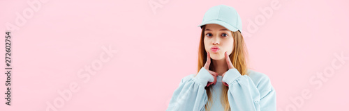 panoramic shot of pretty teenage girl in cap grimacing isolated on pink