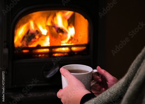 Woman having a hot cup of rink at the fireplace. Burning firepla photo