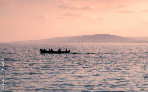 Boat silhouette with man on the water in sunset with mountain in