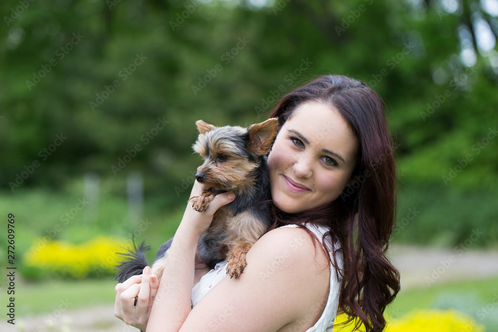 Horizontal medium shot of cute smiling brunette young woman in white top holding small Yorkshire Terrier dog seen in profile Horizontal medium shot of cute smiling brunette young woman in white top holding small Yorkshire Terrier dog seen in profile
