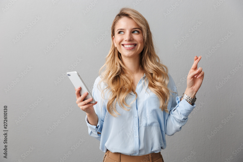 Happy young pretty blonde business woman posing isolated grey wall background using mobile phone. Happy young pretty blonde business woman posing isolated grey wall background using mobile phone.