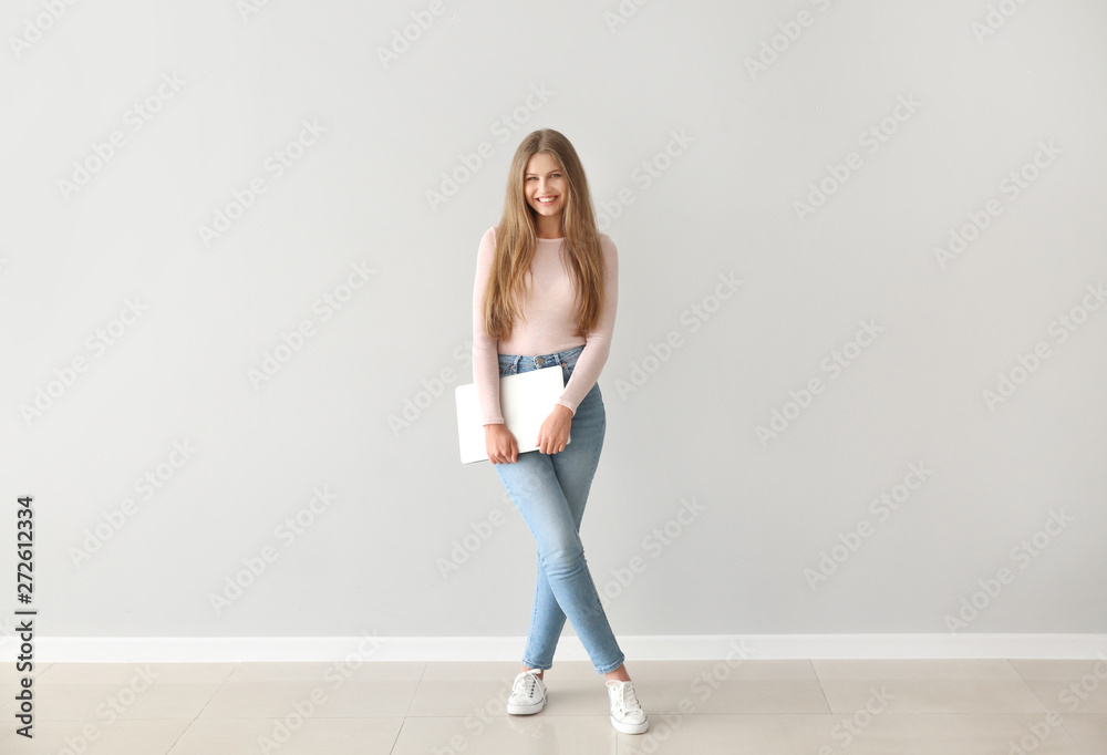 Beautiful young woman with laptop against light wall