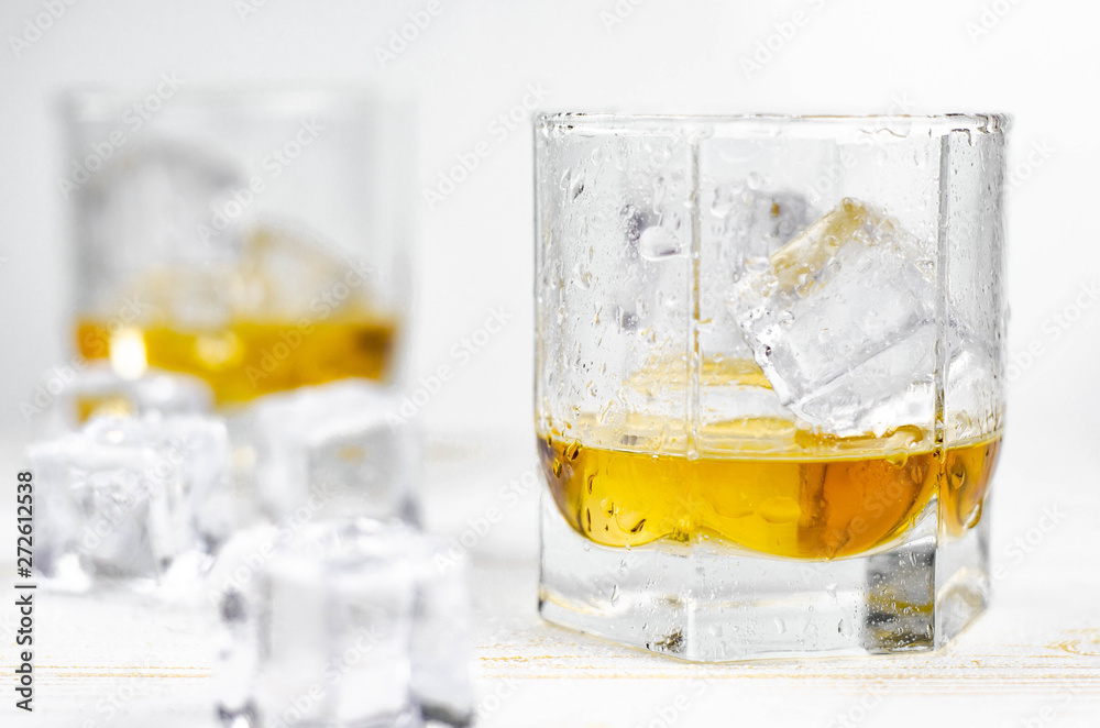 Two glasses of scotch whiskey with ice cubes, white background, wooden backdrop Two glasses of scotch whiskey with ice cubes, white background, wooden backdrop