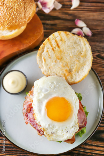 Tasty burger with bacon and fried egg on table