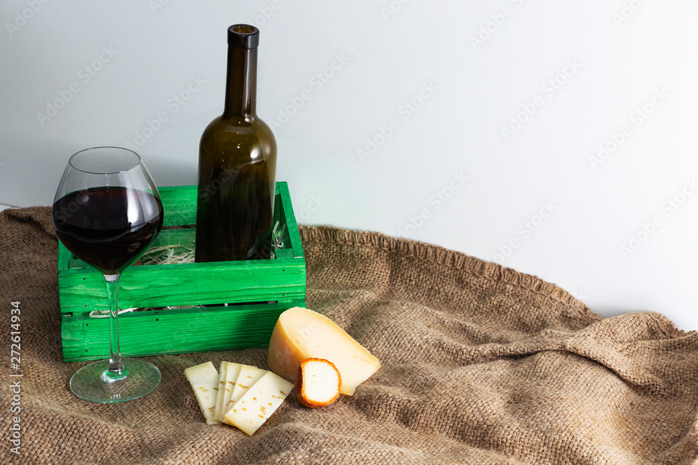 A bottle of red wine with a glass and a piece of cheese.