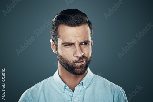 What to do? Confused young man looking away while standing against grey background