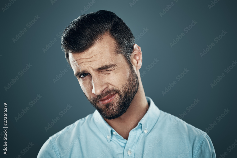 Winking. Handsome young man looking at camera and winking while standing against grey background Winking. Handsome young man looking at camera and winking while standing against grey background