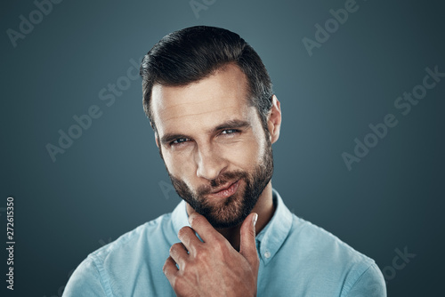 Real macho. Handsome young man smiling and looking at camera while standing against grey background