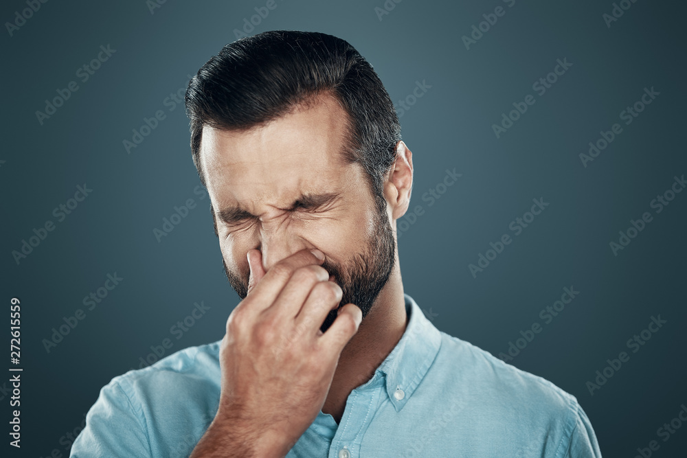Allergy. Handsome young man covering nose with hand while standing against grey background Allergy. Handsome young man covering nose with hand while standing against grey background