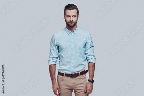 Charming man. Handsome young man looking at camera and smiling while standing against grey background