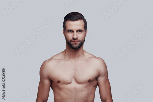 Portrait of confidence. Handsome young man looking at camera and smiling while standing against grey background