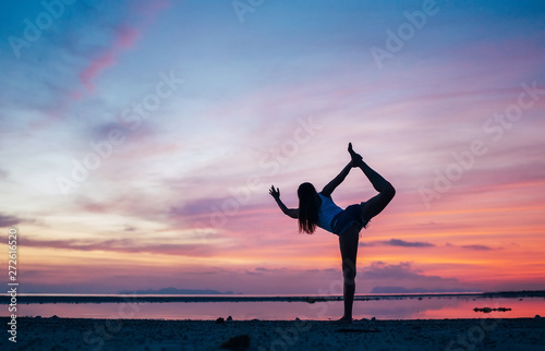 Young Girl making natarajasana yoga pose on the sunset seaside. Active day beginning concept image.