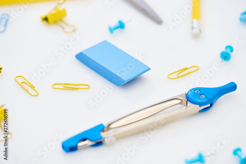 selective focus of blue compasses, eraser and paper clips mixed with yellow paper clips and pencil on white background